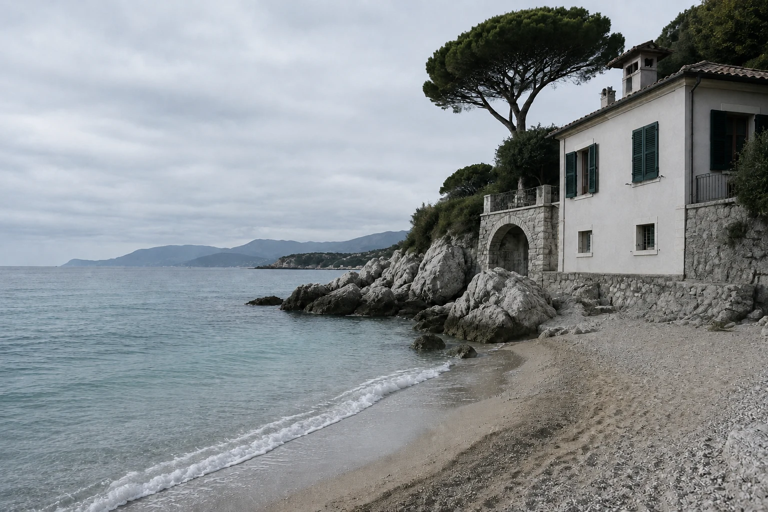 A seaside house with a grey facade and an empty beach under overcast skies